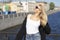 European girl with blond hair enjoys a great sunny day. Standing on the bridge. In the background the buildings and the river