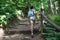 European girl climbs up the natural stairs in summer forest, hiking route, rear view, copyspace
