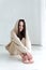 European girl in sweatpants and a hoodie sits on a white wooden floor in a bright room