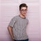 European glamorous stylish young hipster man in fashionable glasses with trendy hairstyle in a youth striped t-shirt posing near a