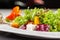 European Italian salad of lettuce, cherry tomatoes, pumpkin, edible pumpkin flowers, and pumpkin seeds, in a white plate.