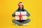 European lady holding festive present box sitting in yellow studio