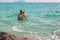 A European man stands chest deep in water and photographs seascapes on a video camera, a blogger prepares materials