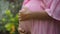 European pregnant girl in a pink dress gently touches her big stomach with her hands, stands on the back green garden