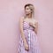 European pretty young blonde woman in a summer stylish striped sundress rests near a pink vintage wall in the city.