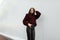 European pretty young fashionable woman in a stylish burgundy sweater in trendy black leather pants posing in the city near a