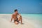 European tanned man wearing swimming shorts sitting at tropical sandy beach at island luxury resort