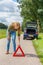 European woman placing hazard warning triangle on road