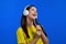 European woman singing with hair brush or comb instead microphone at blue studio background. Lady in headphones having