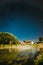 Evaporation Over River Lake Near Houses In Village. Milky Way Galaxy In Night Starry Sky Above Lake River Landscape At