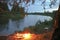 An evening bonfire burns on the bank of a river among a birch forest.