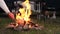 Evening bonfire close-up near the campsite. A man throws firewood