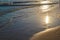 Evening calm waves in the sand. The sun is reflected in the water.