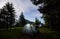 Evening camping at mountains. Friends are sitting near tents in which light is on between fir trees under evening sky