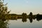 Evening lake summer scenery with sunset and sky reflection on the surface and reeds of water in front.