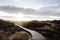 Evening landscape photo against sun. Grassy nature with tourist pathway and distant lighthouse