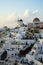 Evening light scene of Oia windmill and white building townscape along island mountain facing ocean with soft cloud and light blue