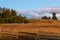 Evening light on wood fence and pasture with trees on hilltop, sky with clouds, Eastern Washington State, USA