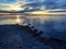 Evening shore of the lake, the sun is setting below the horizon, stones going deep into the lake from the shore