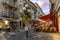 Evening shot of shops and a restaurant with tables, chairs and people on the sidewalk of a street in Nice, France