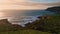 Evening surf washing hills with low greenery. Calm water rolling sunny cliffs