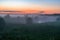 Evening thick fog over field and forest. Landscape of the evening sky with fog, orange and blue sky.