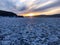 Evening view. Cracks on the surface of the blue ice. Frozen lake Baikal in winter mountains. It is snowing. The hills of pines. Ca