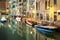 Evening view of illuminated old architecture, floating boats and light reflections in canals water in Venice, Italy