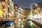 Evening view of illuminated old architecture, floating boats and light reflections in canals water in Venice, Italy