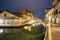 Evening view of illuminated old architecture, floating boats and light reflections in canals water in Venice, Italy