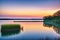 The evening view shows waves on the lake, reeds in the water and trees on the shore.