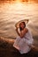 evening walk along the river at a fiery orange sunset, a woman in a dress and a hat sits at the edge of the surf