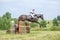 Eventing: equestrian rider jumping over an a brance fence obstacle