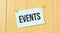 EVENTS sign written on sticky note pinned on wooden wall