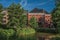 Evergreen garden and pond with mansions on blue sunset sky in Tielt.