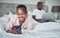 Everybodys got a favourite device. a happy young woman using a smartphone while her husband uses a laptop in bed at home