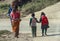 Everyday life in Nepal, children in uniform walk hand in hand to school, mother carries a small child on her back.