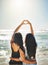 Everyone loves summer. Rearview shot of two friends forming a heart shape together on the beach.