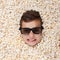 Evil ferocious young boy in stereo glasses looking out of popcorn