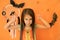 An evil girl intimidating with her formidable appearance in the guise of a witch on an orange background with a Halloween decor