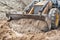 The excavator backfills the pit with the front bucket. Moves soil around the construction site. Close-up. Heavy construction