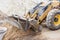 The excavator backfills the pit with the front bucket. Moves soil around the construction site. Close-up. Heavy construction