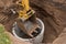 Excavator with a bucket, lowering into the pit on steel cables concrete sewer ring. Construction or repair of sewer home