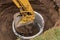 Excavator with a bucket, lowering into the pit on steel cables concrete sewer ring. Construction or repair of sewer home