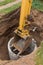 Excavator with a bucket, lowering into the pit on steel cables concrete sewer ring. Construction or repair of sewer home