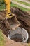 Excavator with a bucket, lowering into the pit on steel cables concrete sewer ring. Construction or repair of sewer home