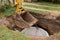 Excavator with a bucket, lowering into the pit on steel cables concrete sewer ring. Construction or repair of sewer home