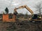 Excavator destroying brick house on land in countryside. Bulldozer clearing land from old bricks and concrete from walls with dirt