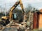 Excavator destroying brick house on land in countryside. Bulldozer clearing land from old bricks and concrete from walls with dirt