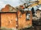 Excavator destroying brick house on land in countryside. Bulldozer clearing land from old bricks and concrete from walls with dirt